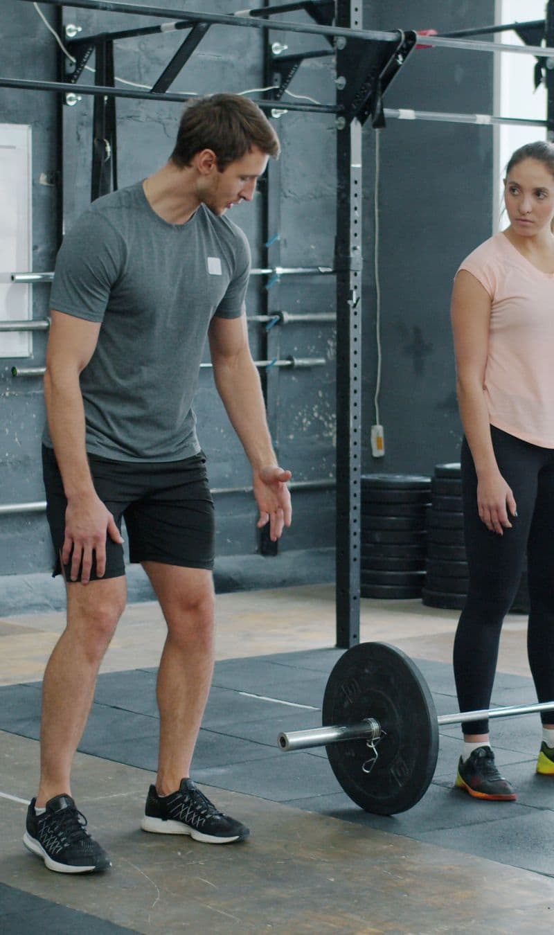 A coach talking a client through a barbell setup in a bright studio