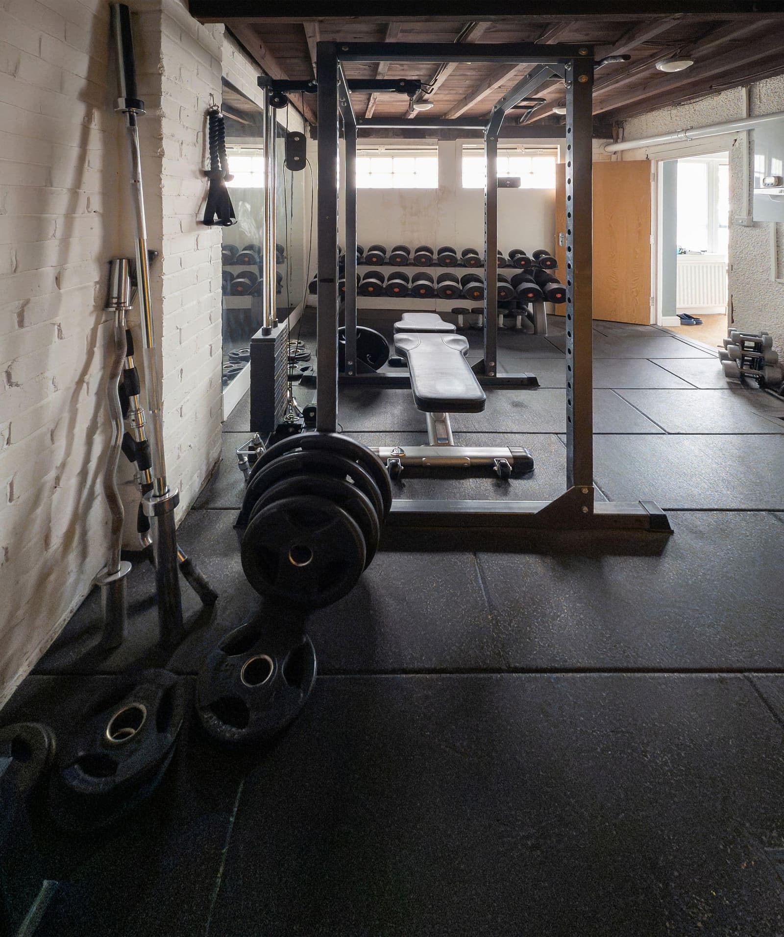 A small private studio with a squat rack, bench and plates on a rubber floor